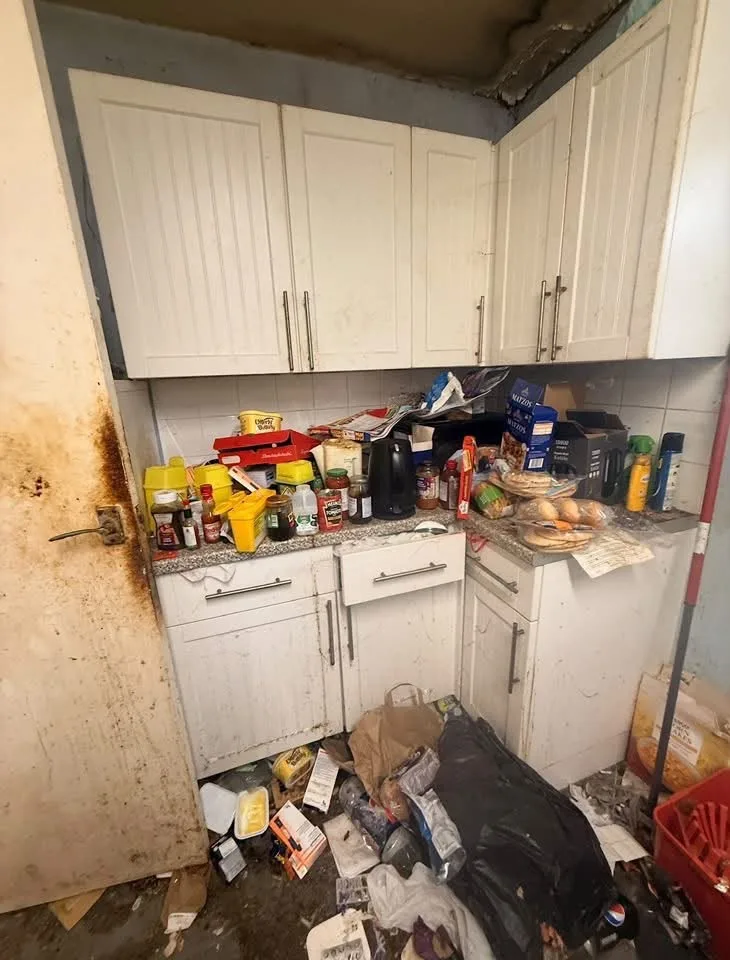 Kitchen corner before cleaning: a cluttered worktop, rubbish on the floor and a stained door.