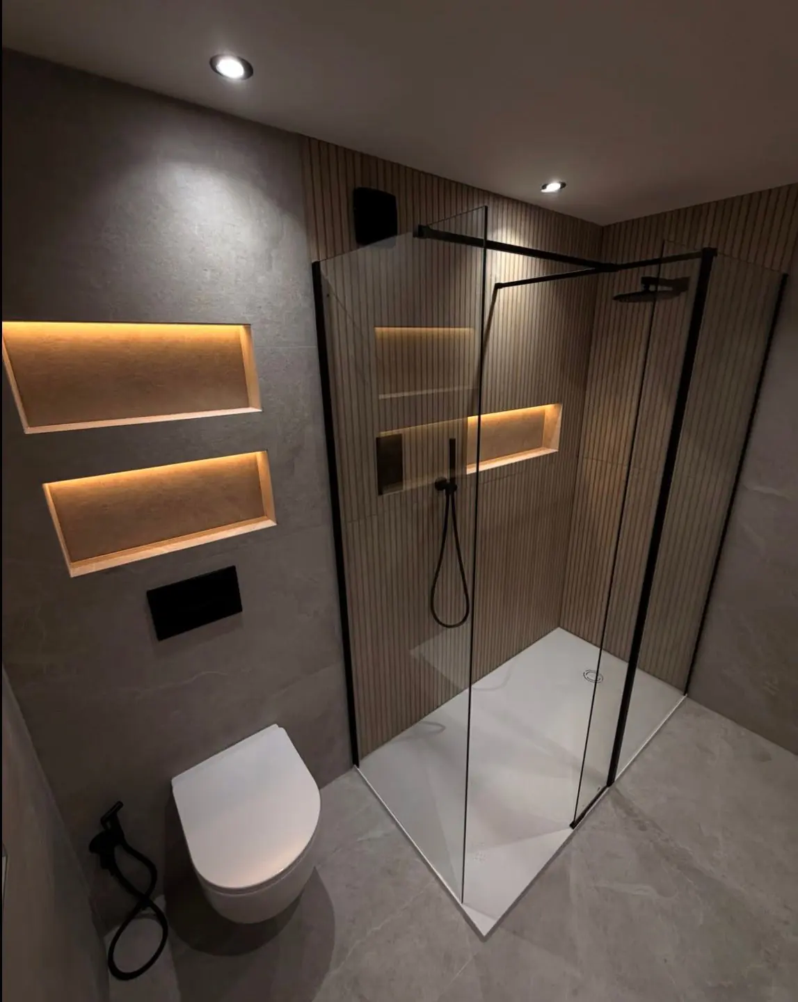 Bathroom with a slatted wood shower wall, warm-lit shelves and a wall-hung toilet